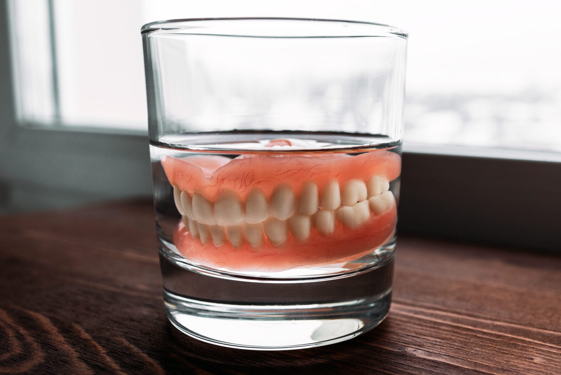 A denture in a glass of water. Dental prosthesis care. Full removable plastic denture of the jaws. Two acrylic dentures. Upper and lower jaws with fake teeth. Dentures or false teeth, close-up.