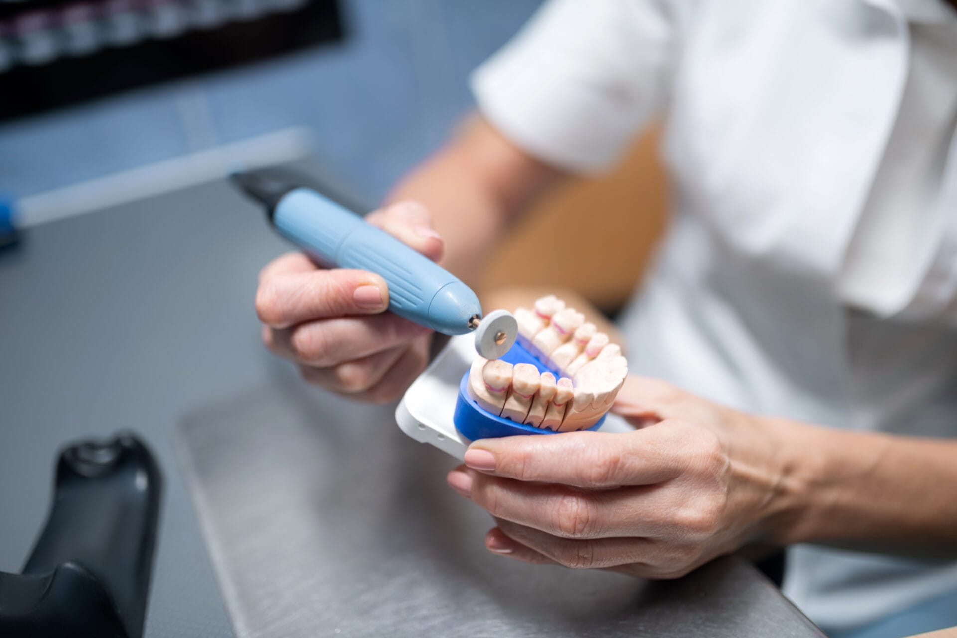 Dental prosthesis in hands of professional dental technician polishing it on her table